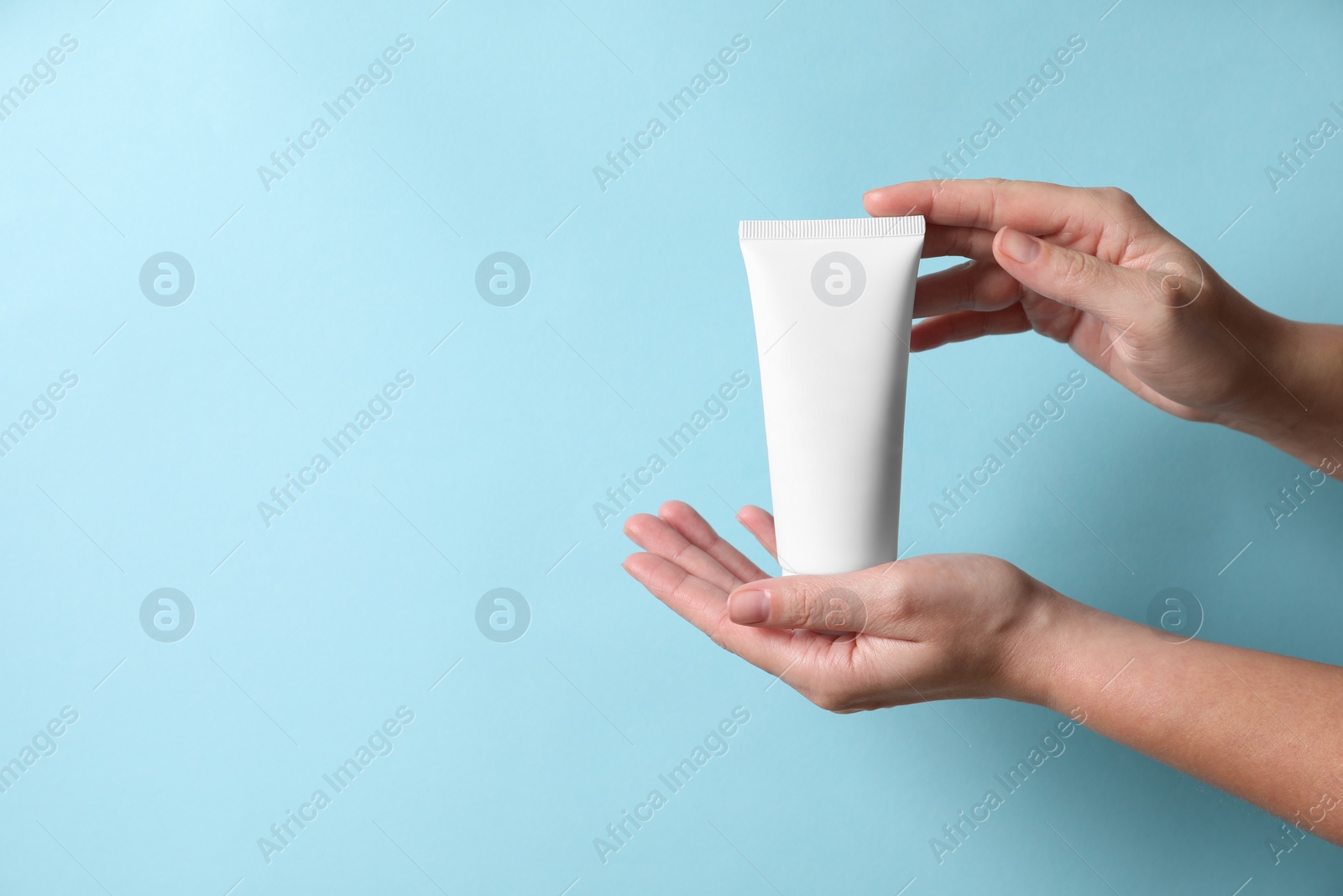 Photo of Woman with tube of hand cream on light blue background, closeup. Space for text