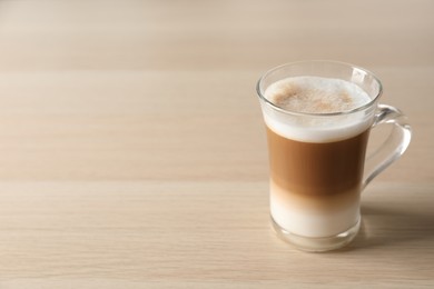 Hot coffee with milk in glass cup on wooden table. Space for text