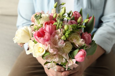 Photo of Man holding bouquet of beautiful flowers indoors, closeup