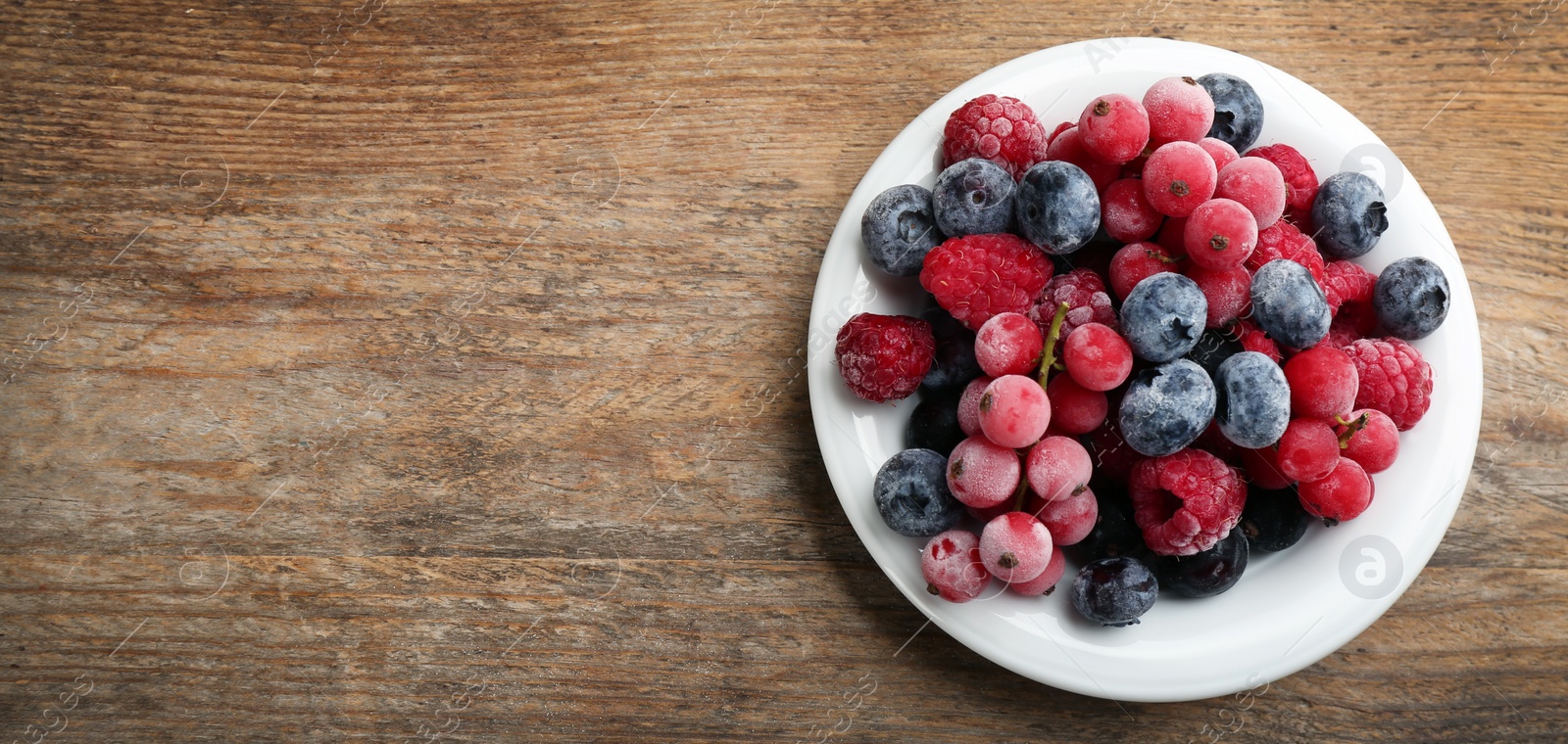 Photo of Mix of tasty frozen berries on wooden table, top view. Space for text