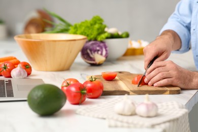 Man making dinner while watching online cooking course via laptop at table, closeup