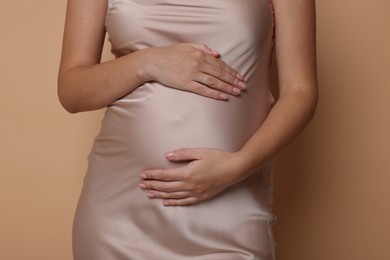 Pregnant woman in dress on beige background, closeup