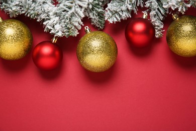 Christmas balls and fir tree branches with snow on red background, flat lay. Space for text