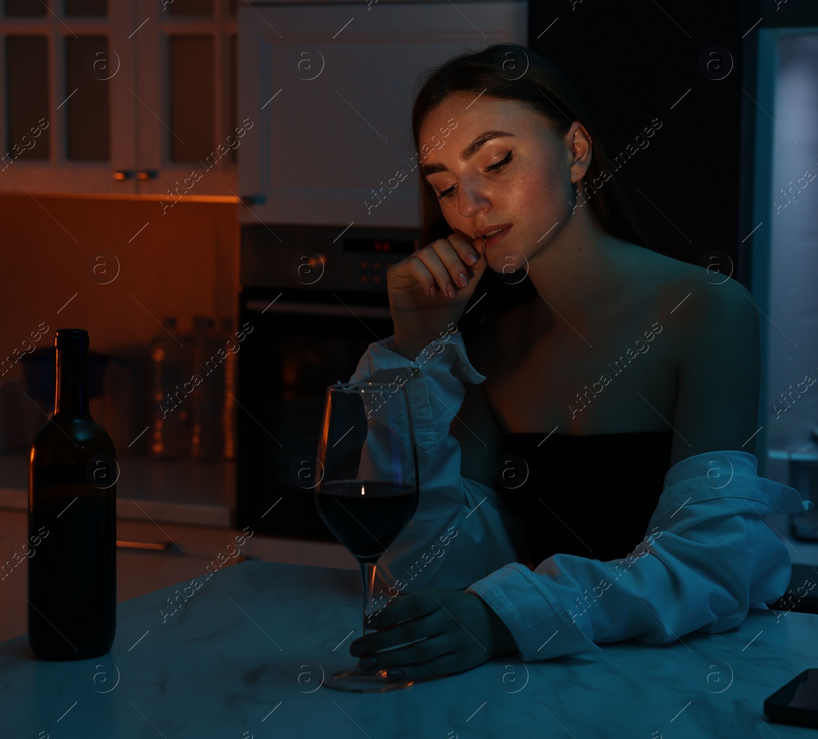 Photo of Beautiful woman chilling with glass of wine in kitchen at night