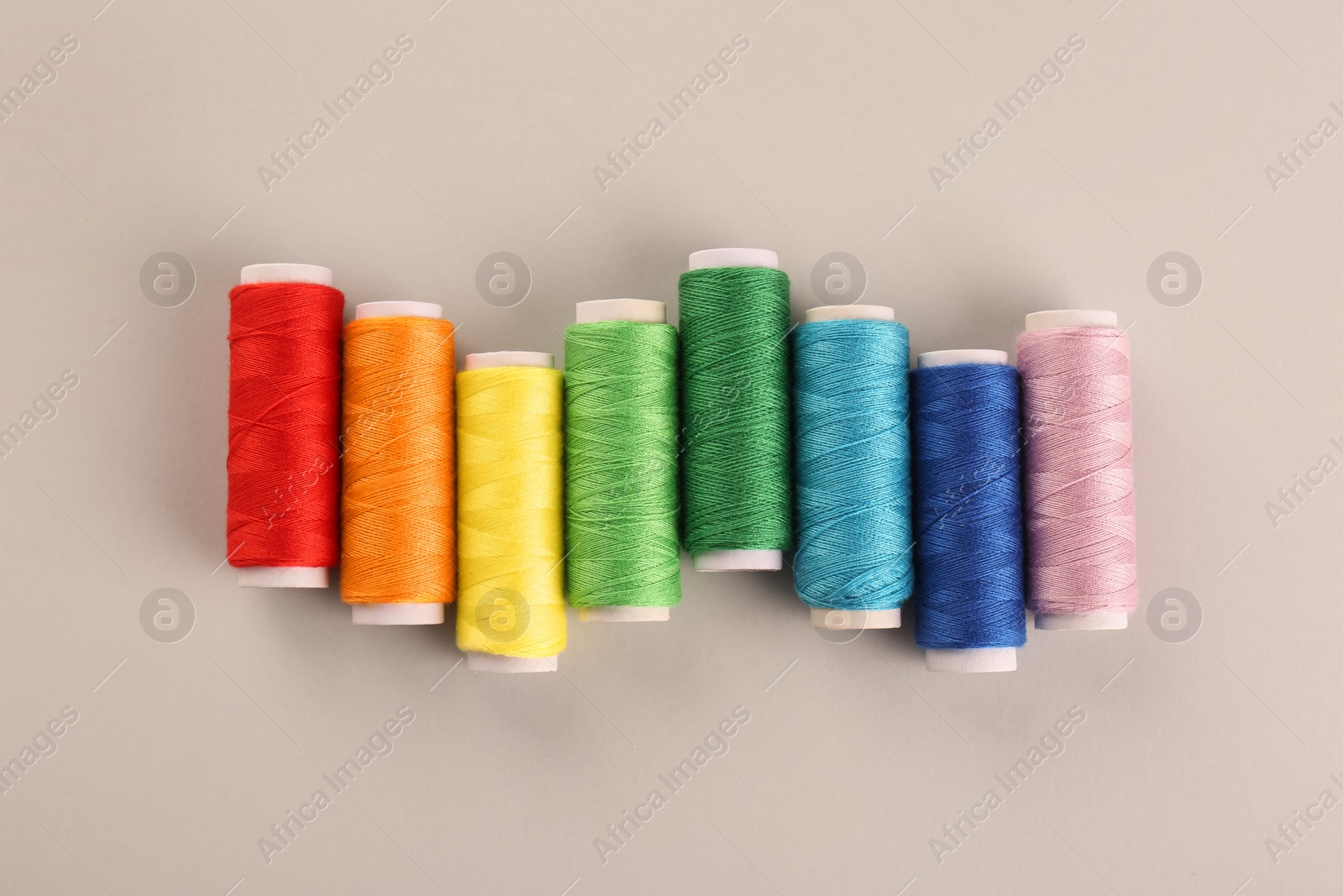 Photo of Different colorful sewing threads on light grey background, flat lay