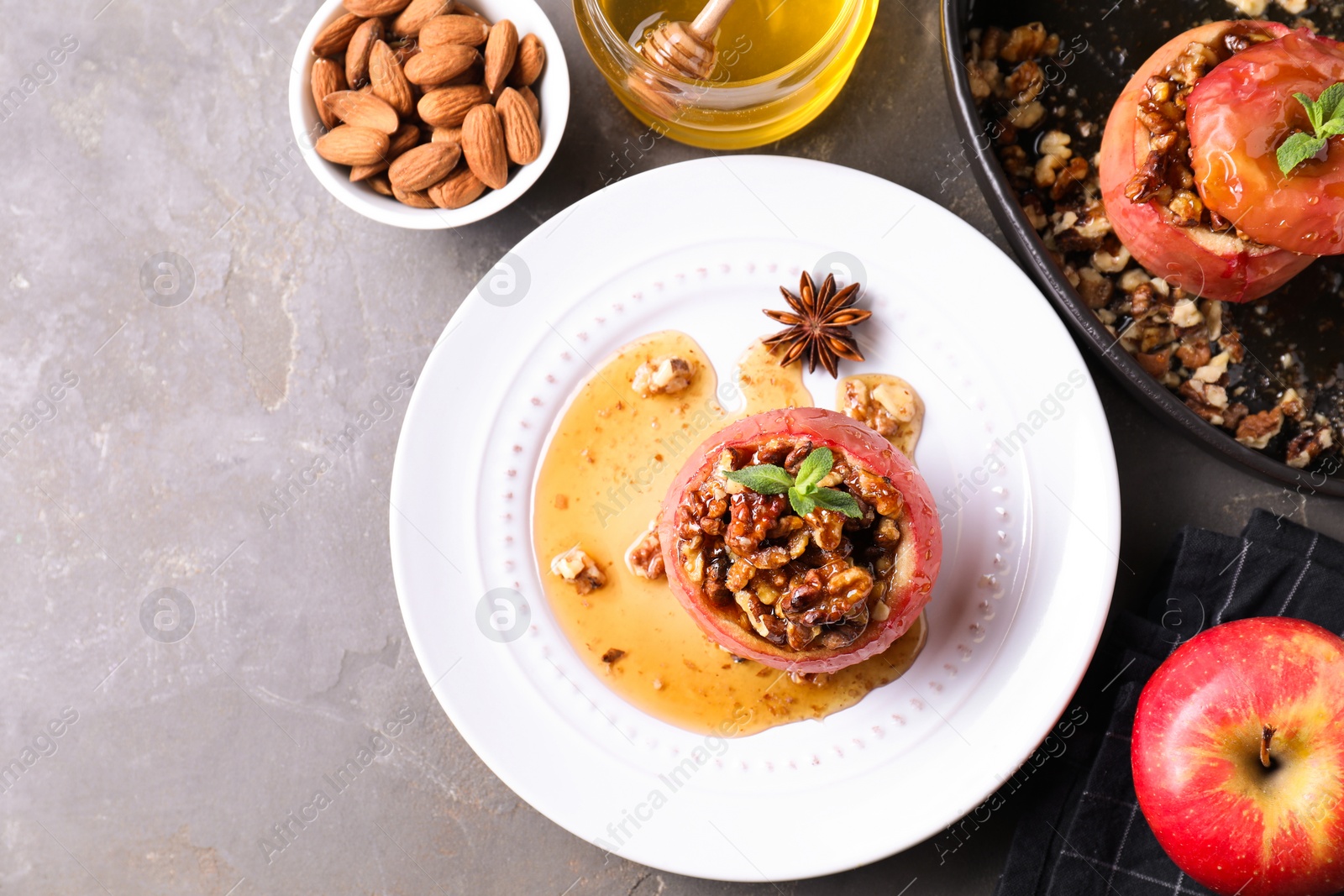 Photo of Tasty baked apples with nuts, honey and mint on gray textured table, flat lay. Space for text