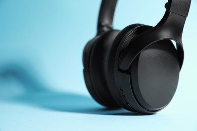 Photo of Modern wireless headphones on light blue background, closeup. Space for text