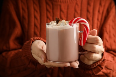 Photo of Woman holding glass cup of tasty cocoa with marshmallows and Christmas candy cane, closeup