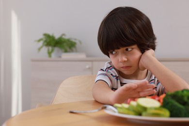 Photo of Cute little boy refusing to eat vegetables at home, space for text
