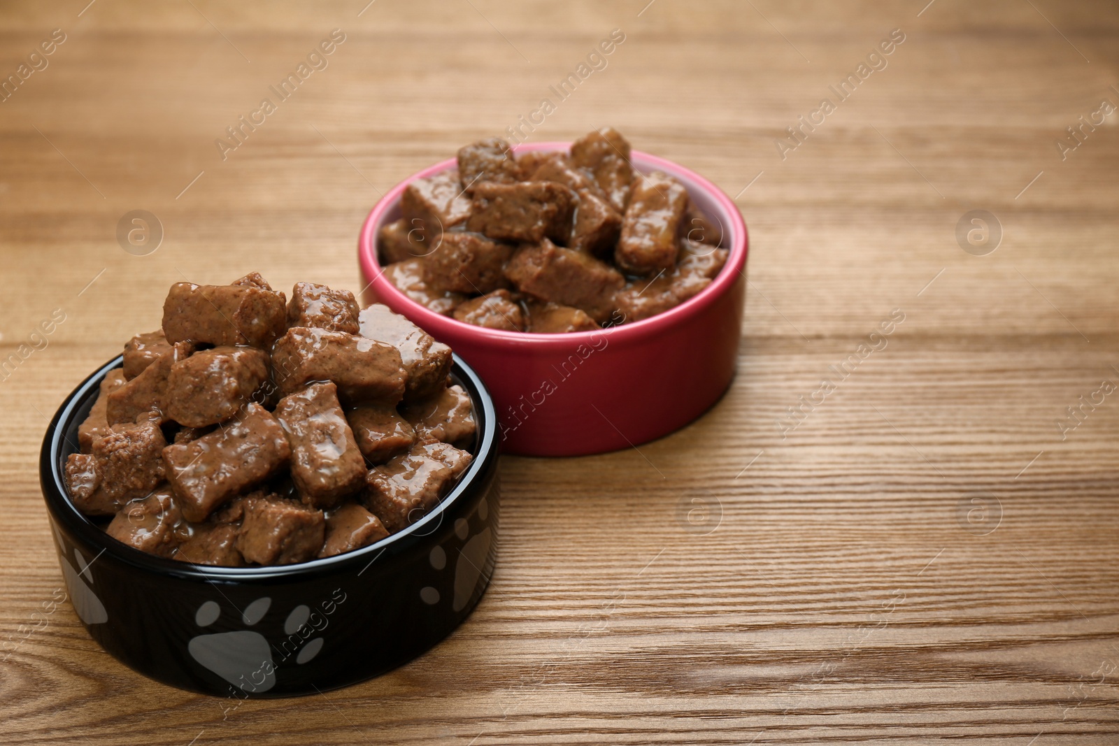 Photo of Wet pet food in feeding bowls on wooden background, space for text