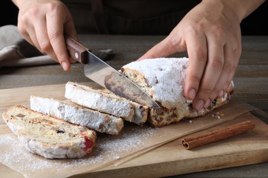 Photo of Woman cutting traditional Christmas Stollen at wooden board, closeup