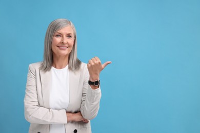 Portrait of beautiful middle aged woman pointing at something on light blue background, space for text