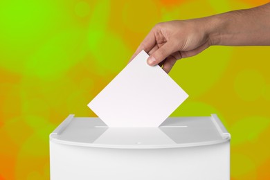 Man putting his vote into ballot box on color background, closeup