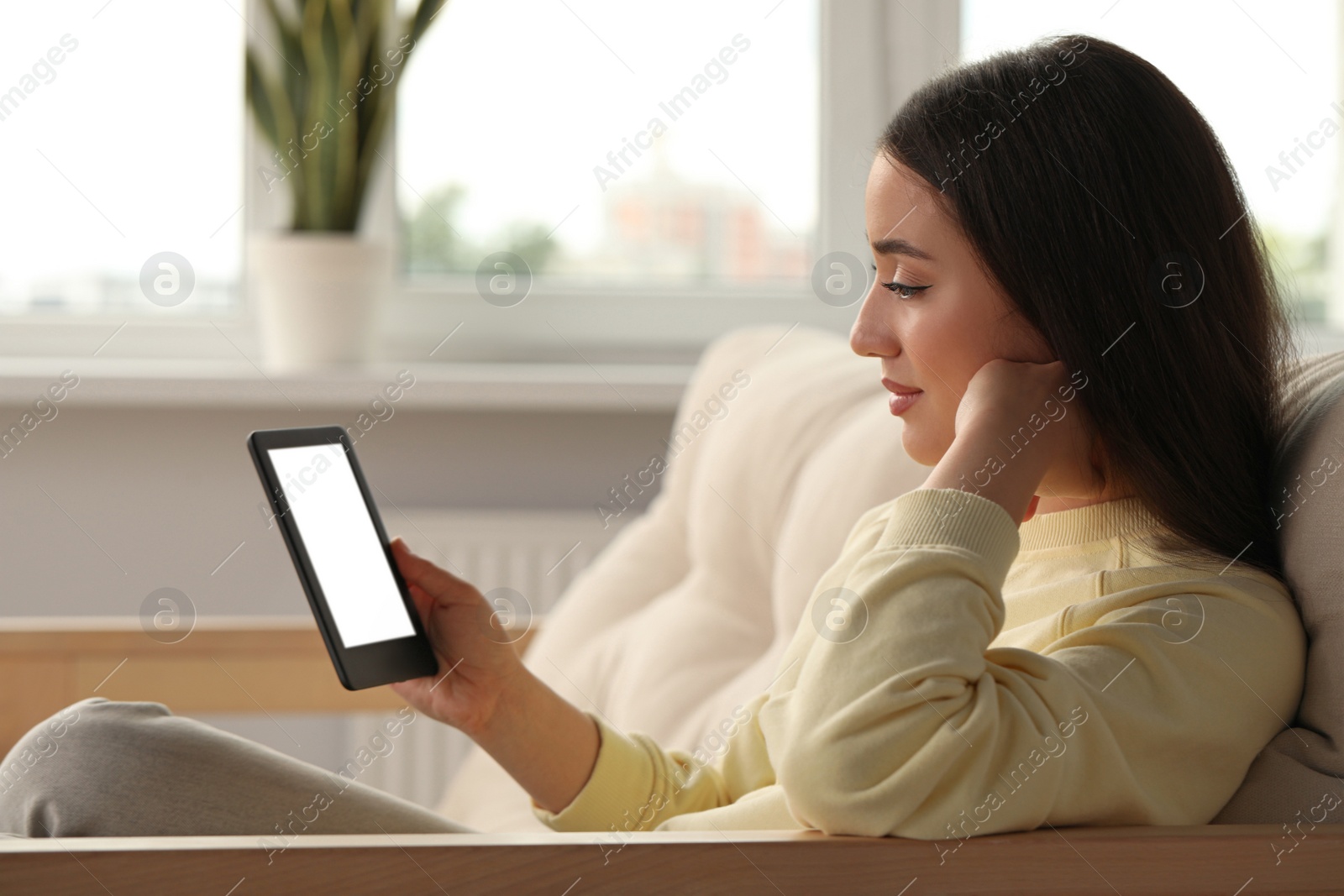 Photo of Young woman using e-book reader at home