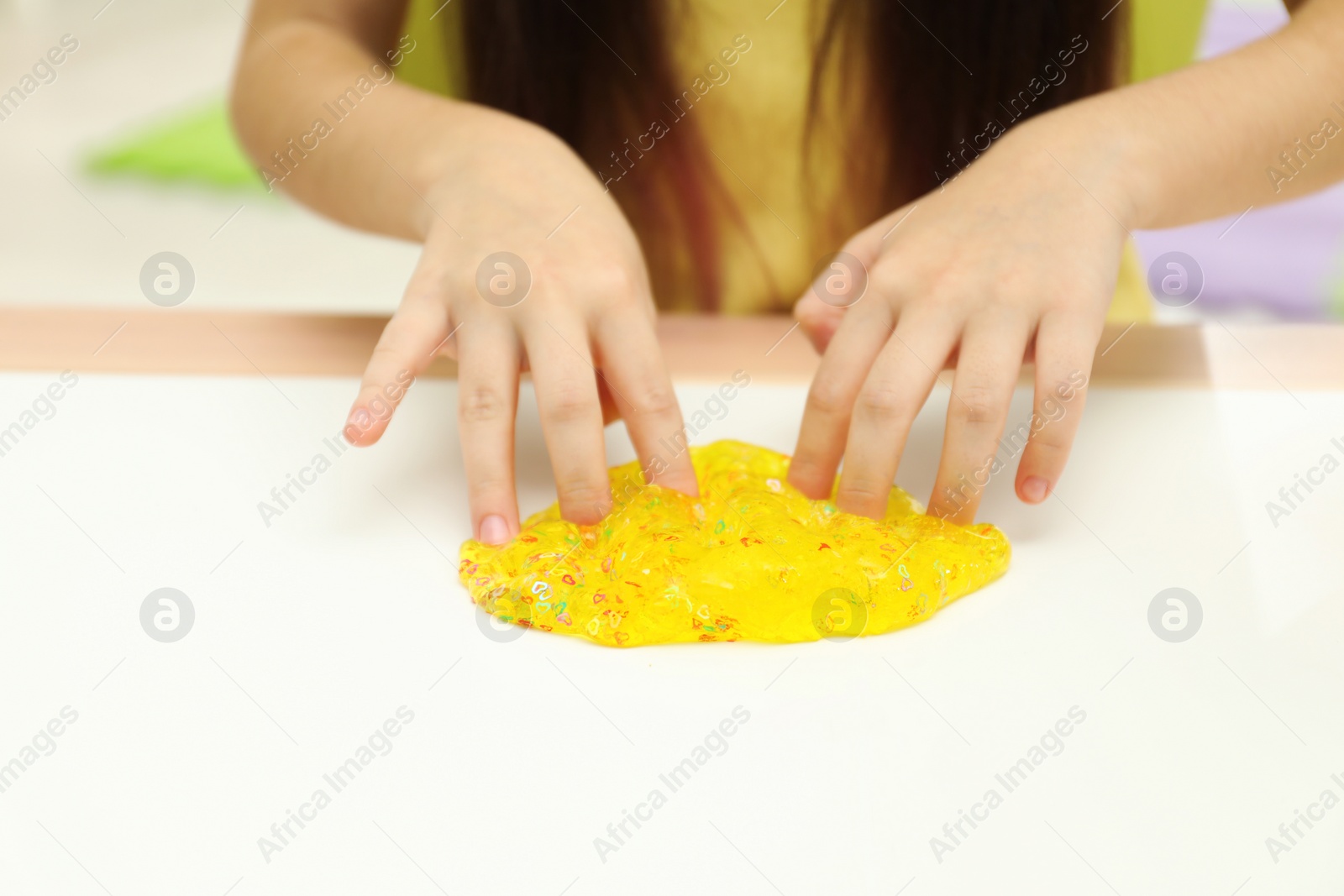 Photo of Little girl playing with slime at white table, closeup