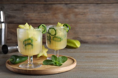 Photo of Glasses of spicy cocktail with jalapeno and carambola on wooden table. Space for text