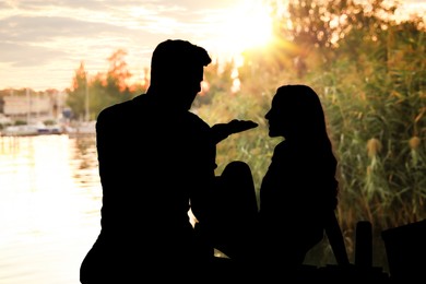 Image of Silhouette of lovely couple spending time on pier outdoors at sunset
