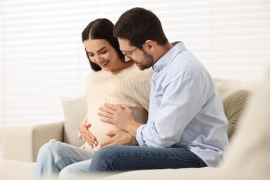 Photo of Happy pregnant woman spending time with her husband on sofa at home