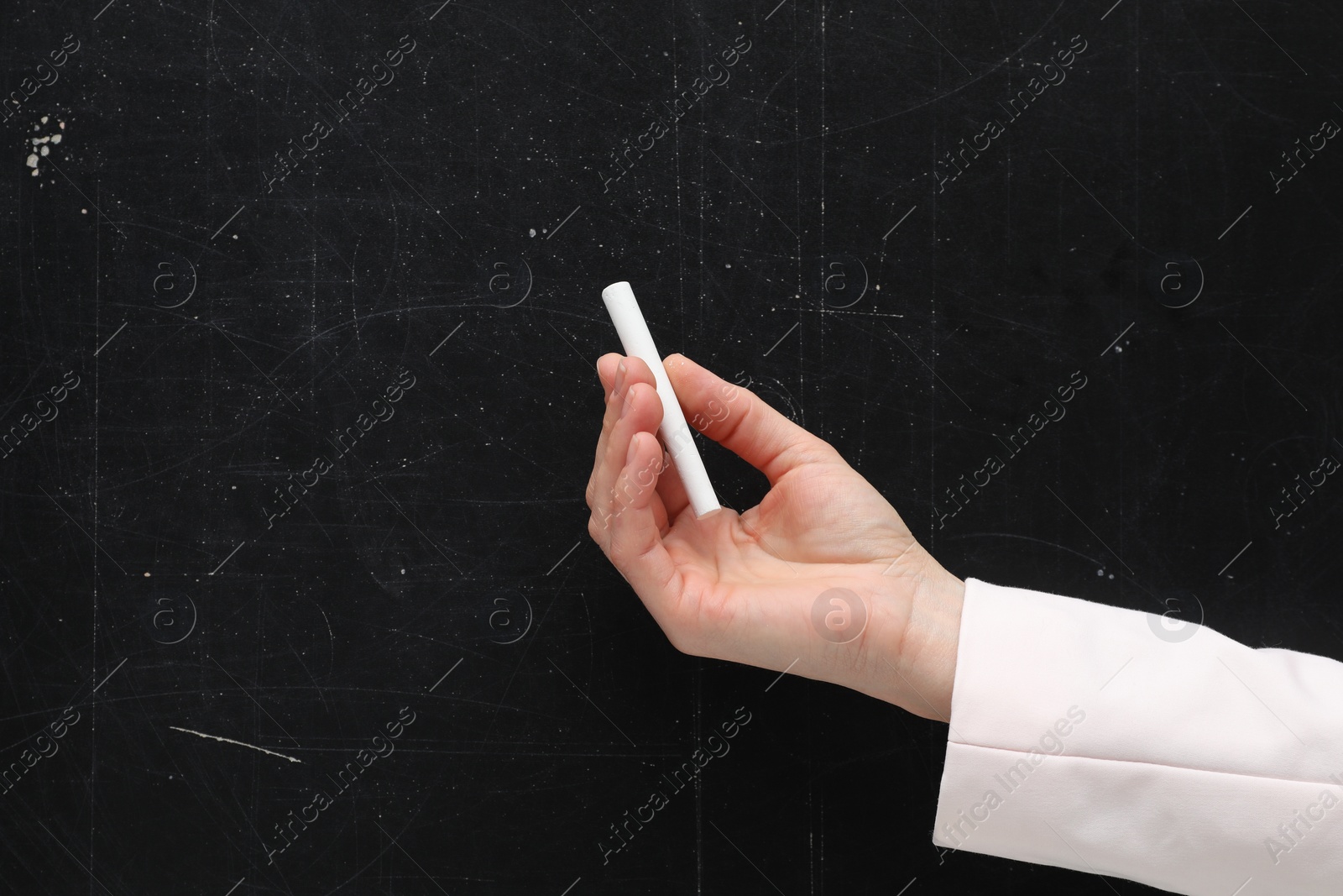 Photo of Teacher writing with chalk on black chalkboard, closeup. Space for text