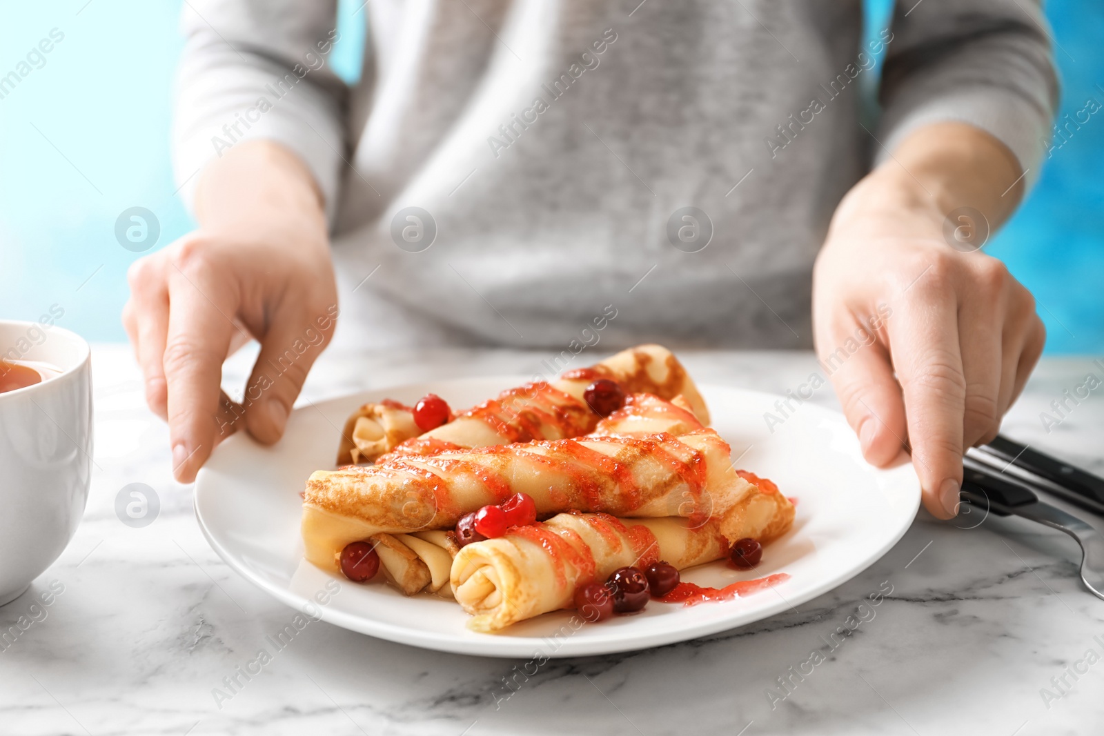 Photo of Woman putting plate with thin pancakes, berries and syrup on table