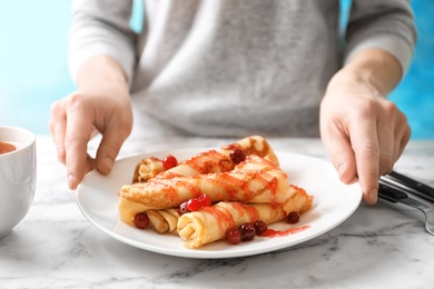 Woman putting plate with thin pancakes, berries and syrup on table