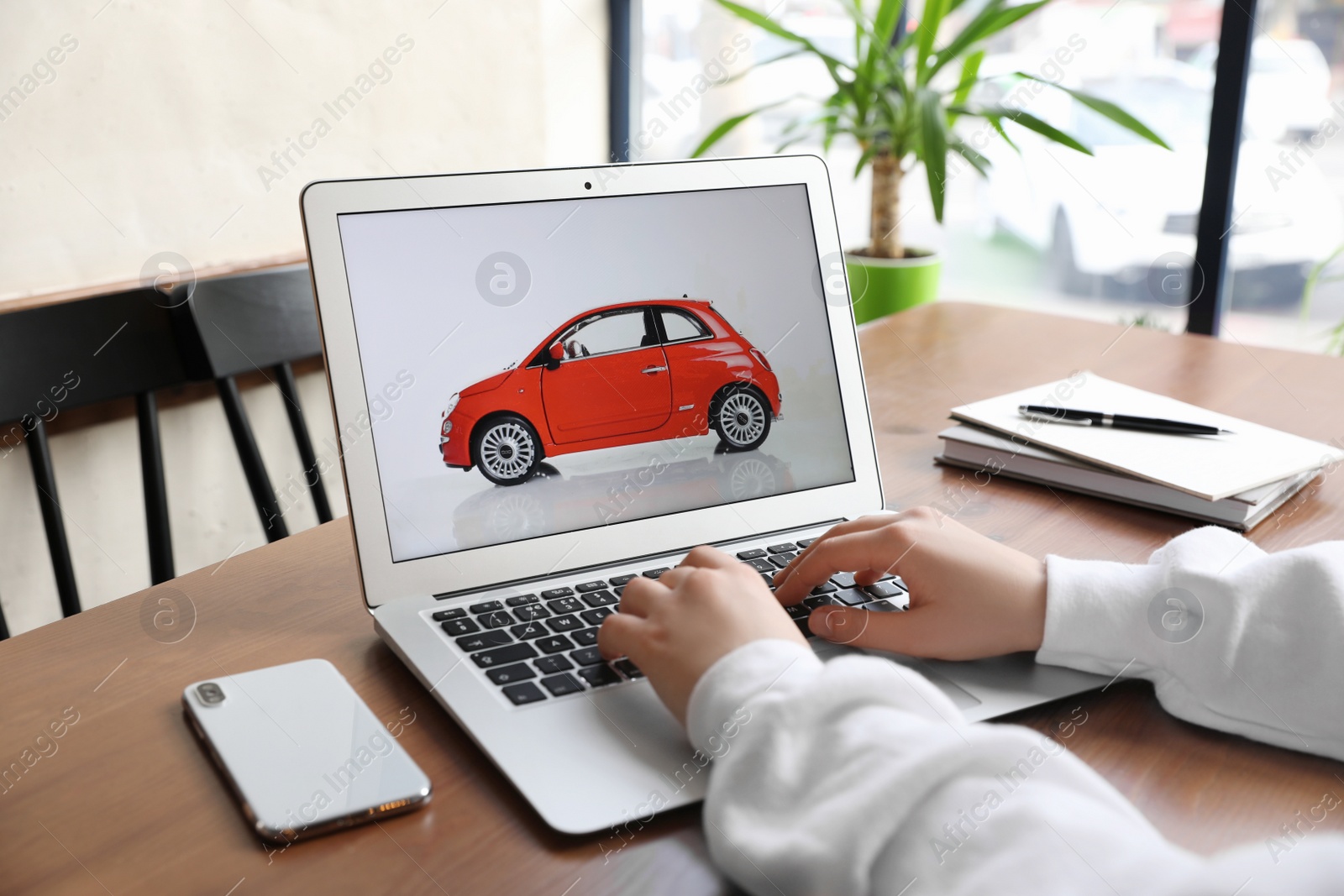 Photo of Woman using laptop to buy car at wooden table indoors, closeup