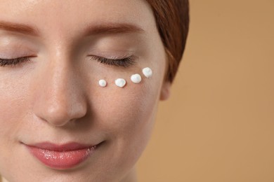 Beautiful woman with freckles and cream on her face against beige background, closeup. Space for text