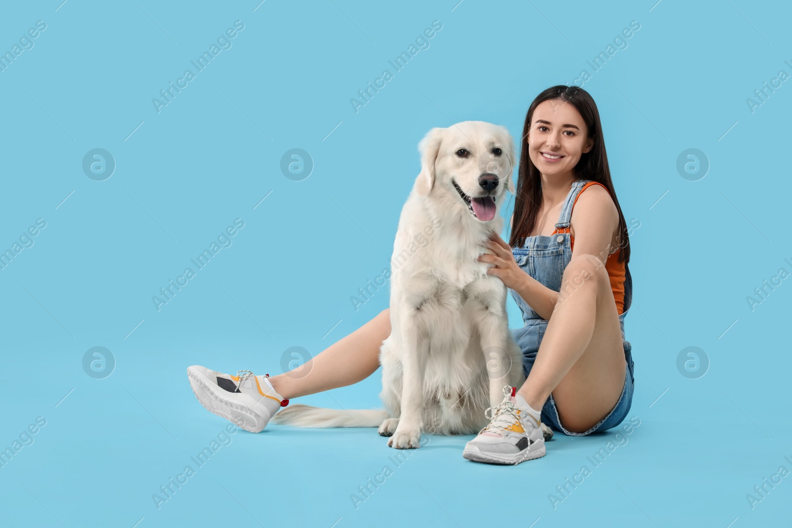 Photo of Happy woman with cute Labrador Retriever dog on light blue background. Adorable pet
