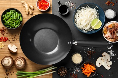 Flat lay composition with black wok surrounded by spices and products on dark table