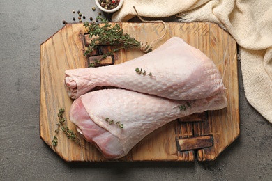 Photo of Board with raw turkey drumsticks, spices and thyme on grey background, top view