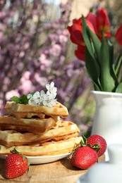 Photo of Freshly baked waffles and beautiful bouquet of tulips on table in garden, closeup