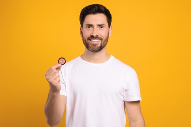 Photo of Happy man holding condom on yellow background. Safe sex