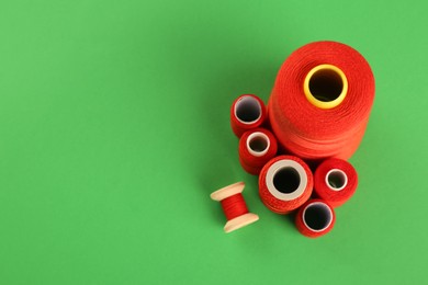 Photo of Red sewing threads on green background, flat lay. Space for text
