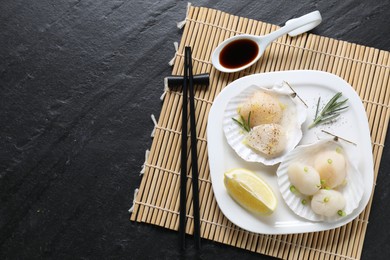 Photo of Raw scallops with green onion, rosemary, lemon and soy sauce on dark textured table, top view. Space for text