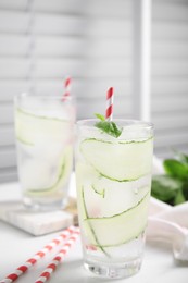 Glasses of refreshing cucumber water with basil on white table