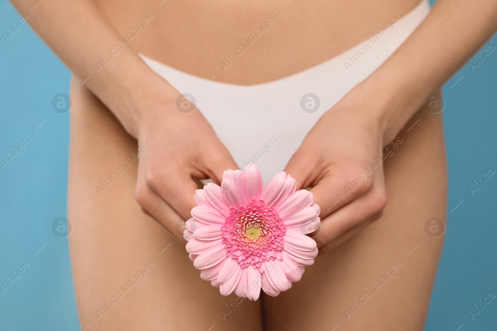 Photo of Woman in white panties with gerbera flower on light blue background, closeup