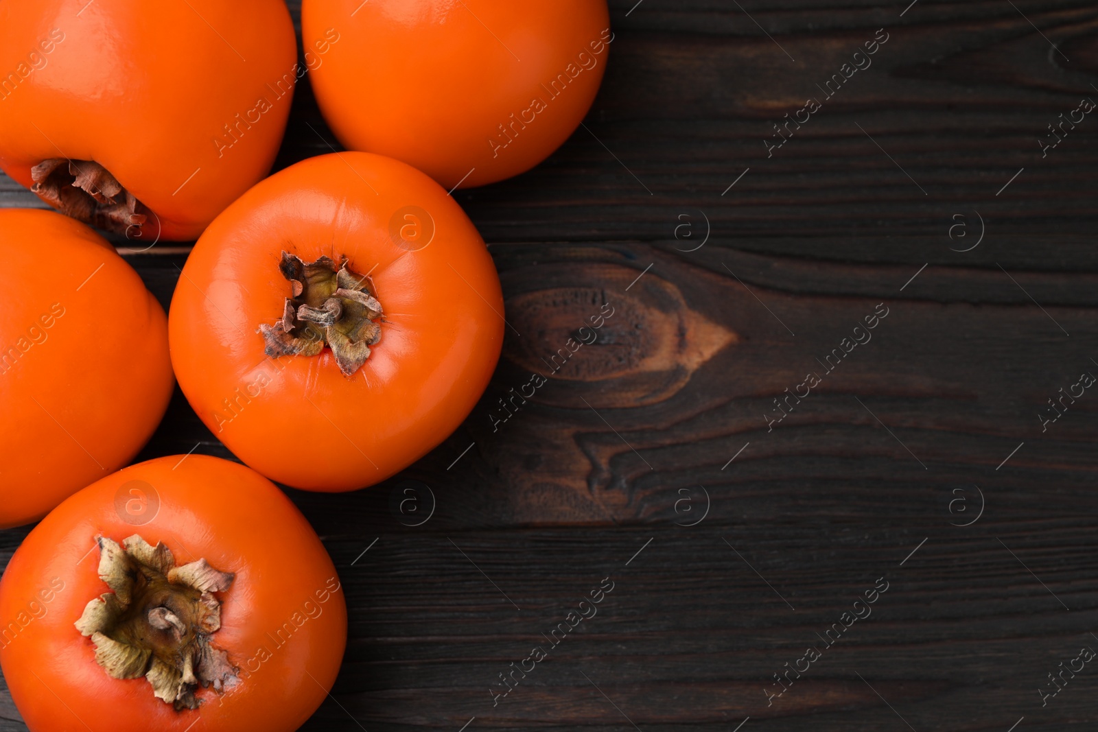 Photo of Delicious ripe persimmons on dark wooden table, top view. Space for text