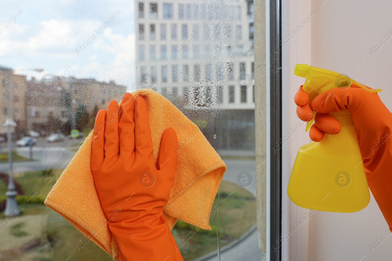 Photo of Young woman cleaning window glass with rag and detergent at home, closeup