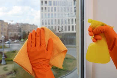 Young woman cleaning window glass with rag and detergent at home, closeup