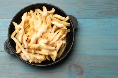 Photo of Delicious french fries with cheese sauce in bowl on light blue wooden table, top view. Space for text