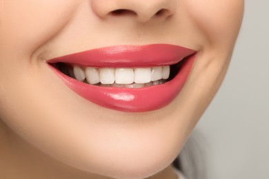 Smiling woman with healthy teeth on light background, closeup