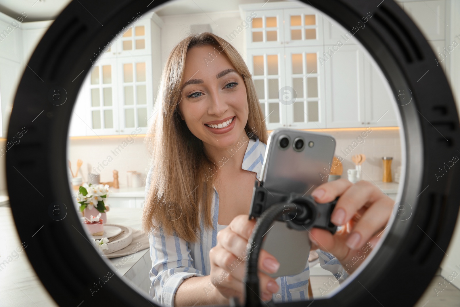 Photo of Blogger preparing for video recording in kitchen at home. Using smartphone and ring lamp