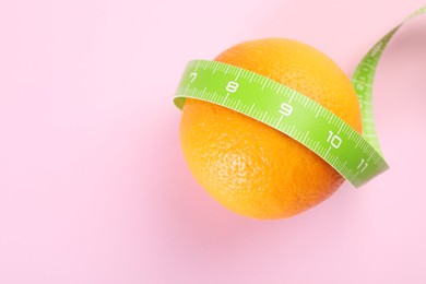 Photo of Cellulite problem. Orange with measuring tape on pink background, top view. Space for text