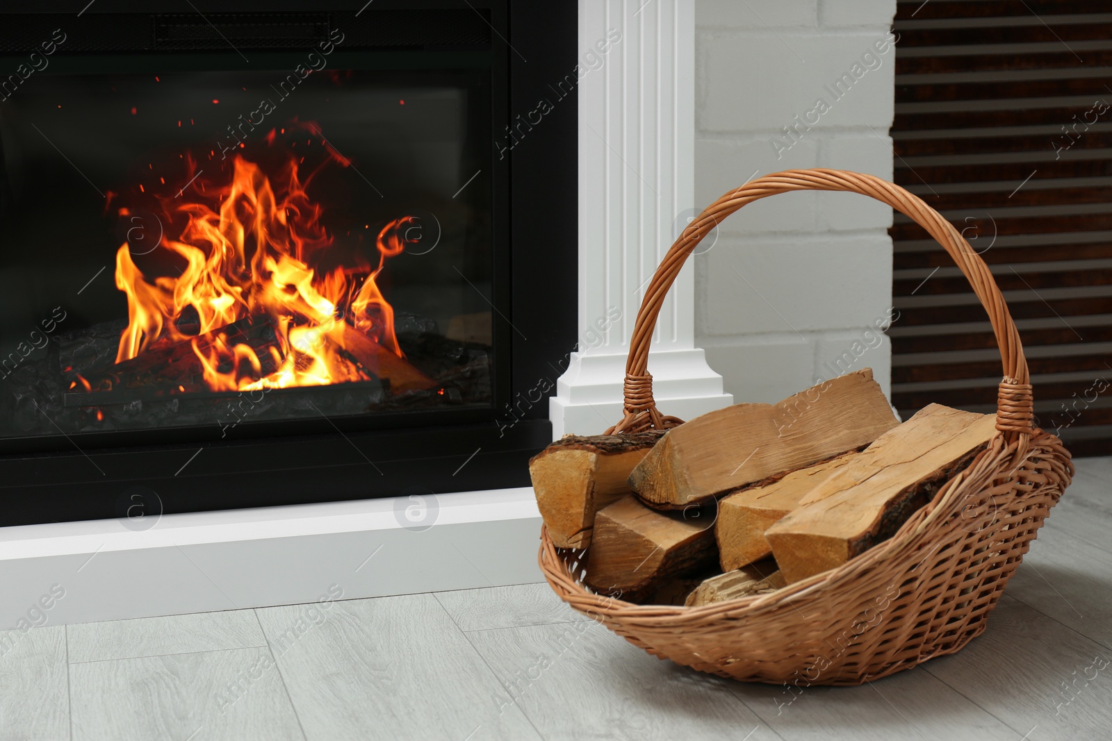 Photo of Firewood in wicker basket near fireplace indoors