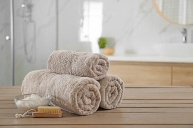 Clean rolled towels, cosmetic salt and brush on wooden table in bathroom. Space for text