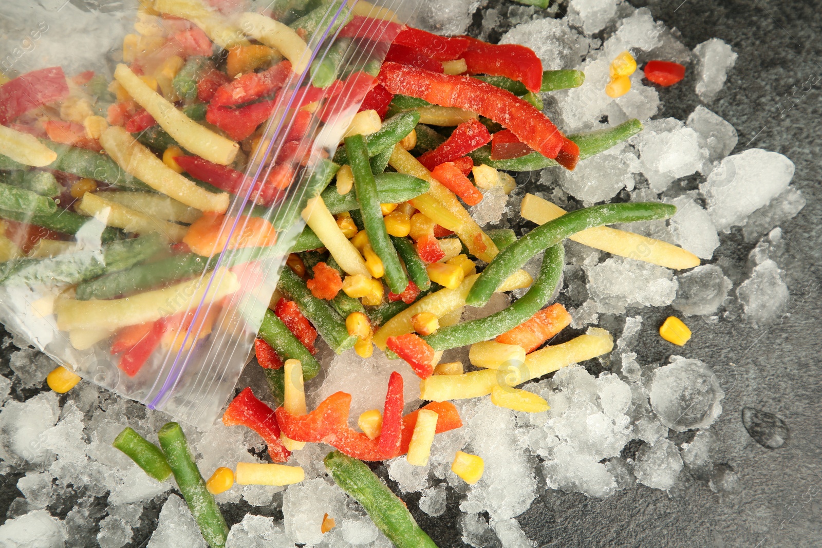 Photo of Zip bag with different frozen vegetables and ice on grey table, top view