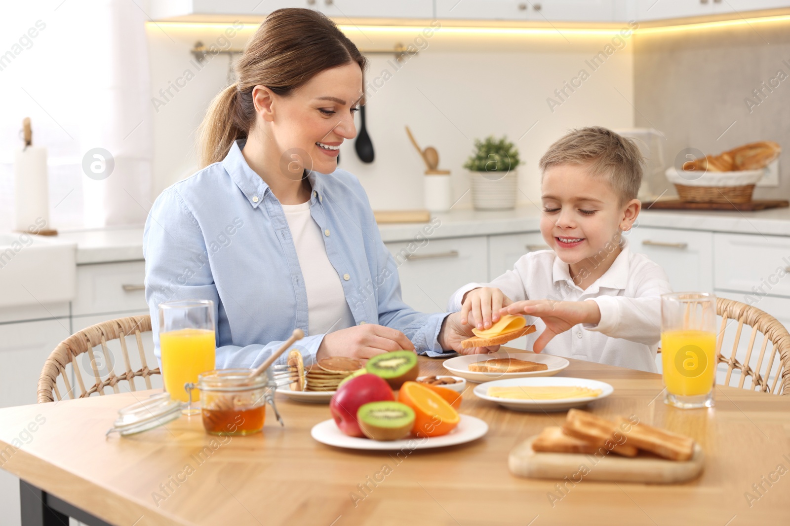 Photo of Mother and her cute little son having breakfast at table in kitchen