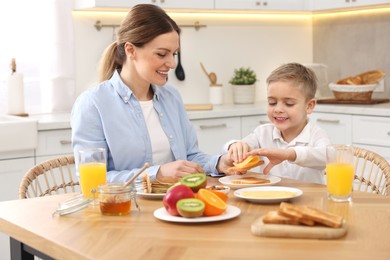 Photo of Mother and her cute little son having breakfast at table in kitchen