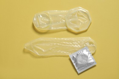 Photo of Unrolled female, male condoms and package on yellow background, flat lay. Safe sex