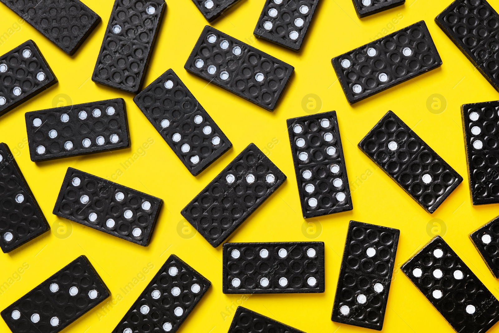 Photo of Black domino tiles on yellow background, flat lay